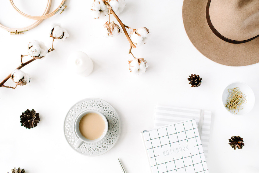 Flat lay trendy creative feminine accessories arrangement with coffee, cotton branch and diary. Hat, cotton branch, notebook, coffee cup, fir cone, golden clips on white background. Top view